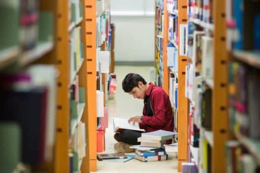 Student reading on the floor of the library in between two bookshelves