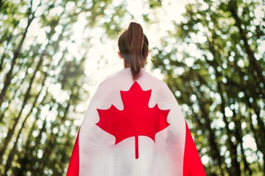 Canadian immigration person standing facing away from the camera with Canadian flag draped over their back