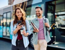 Two students walking off the bus while using their phones and smiling.