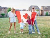 family with kids boy and girl standing in park and holding large Canadian flag