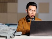 Portrait of a young university student who is doing homework and studying on his laptop in a library