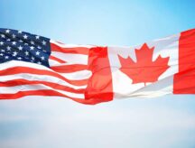 An American and Canadian flag blowing in the wind against one another.