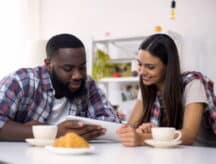 Young couple drinking coffee and choosing vacation trip on tablet