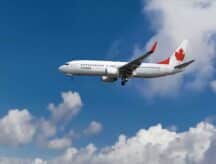 An Air Canada plane traversing the skies, with clouds in the background.