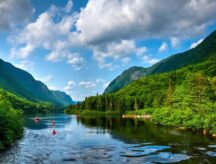 A view of a river in Canada during a summer day, with kayaks and canoes making their way through.