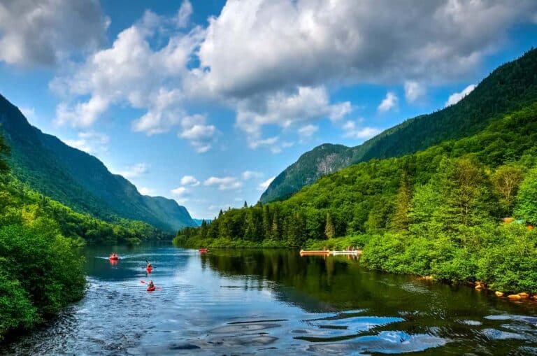 A view of a river in Canada during a summer day, with kayaks and canoes making their way through.