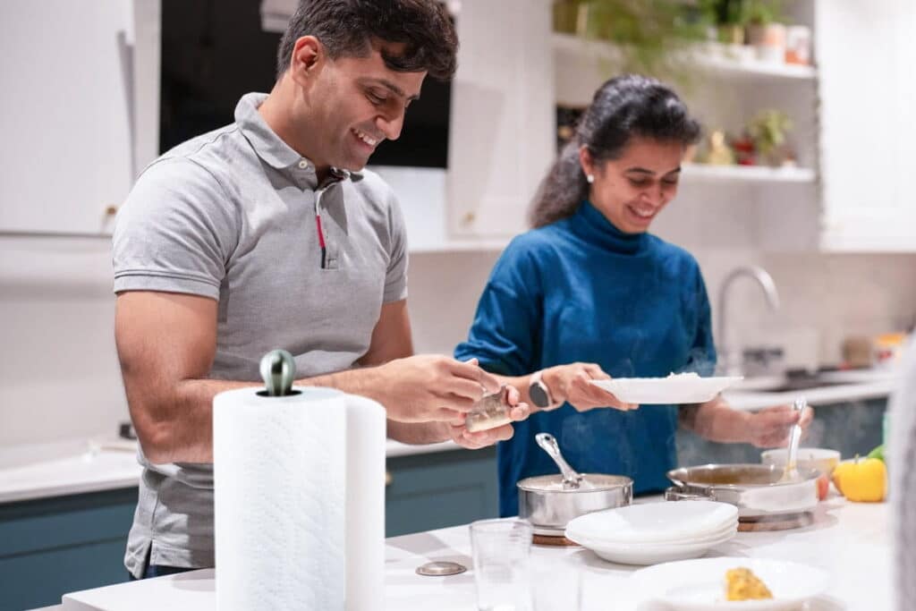 Un hombre y una mujer están de pie junto a una encimera de cocina mientras cocinan, con una toalla de papel a su lado.