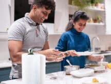 A man and a woman stand next to a kitchen counter while cooking, with a paper towel next to them.