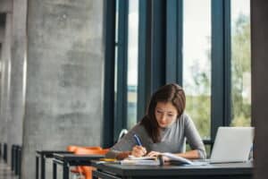 A female student sits at a desk and writes in a big book