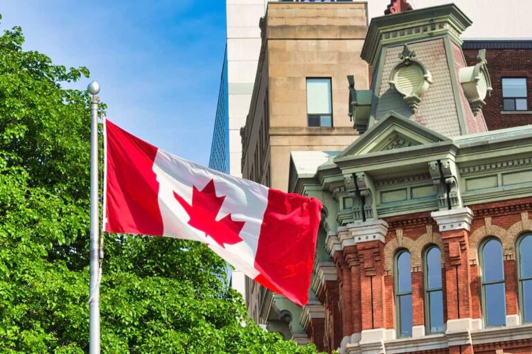 A Canadian flag waving with a tree, and both modern and classical buildings in the background.