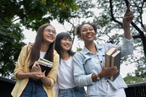 Three international students walk together while carrying books and smiling.