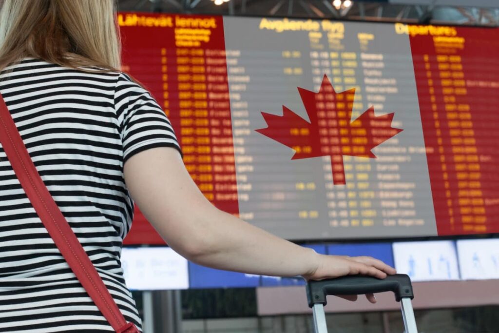 Woman's arm holds suitcase as she stares at a screen depicting flight timings.