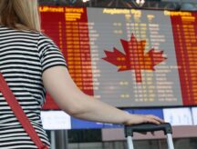 Woman's arm holds suitcase as she stares at a screen depicting flight timings.