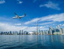 A plane flying past the Toronto skyline on a clear summer day.