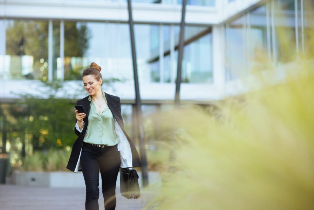 A woman in a suit smiles while checking her phone