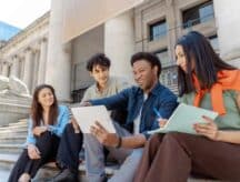 A multicultural group of youths sit on the steps of a building in Toronto, laughing and socializing.