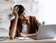 A man looks frustratedly at his laptop, presumably at a study permit refusal from IRCC.