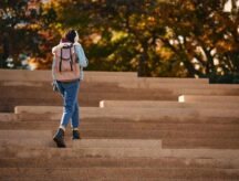 A college student walking on campus steps outside.