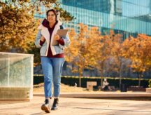 A young woman walks while carrying a laptop