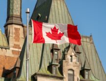 A Canadian flag waving in front of Canada's parliament building