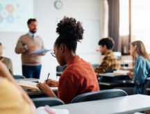 Young woman writing while attending a lecture in the classroom.