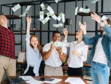 Diverse employees celebrate by throwing money in the air.