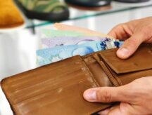 A man holds his wallet filled with Canadian money, in what appears to be a shoe store.