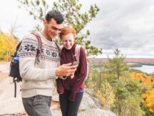 Couple hiking overlooking Northern Ontario forest, looking at mobile phone.