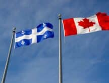 The Quebec provincial flag and the Canadian national flag side by side, blowing in the wind