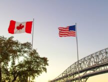 A picture of the Canadian and American flags on either side of the border crossing between Canada and the US