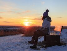 Woman stares at a sunset on a snowy beach.