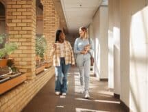 Two women walking down a hallway of their school campus.