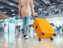 A person rolls a bright yellow suitcase in a well-lit airport set terminal