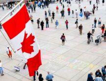 People walking in front of the Canadian flag.