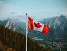 The Canadian flag waving in the wind with snow-speckled mountains in the backdrop.