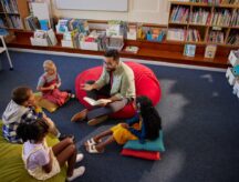 A young teacher reading a book to kindergarten students.